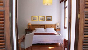 A hotel room with a wooden bed, two bedside tables with lamps, a wooden chair, and three framed pictures on the wall. - Casablanca Koeler Hotel (Petrópolis)