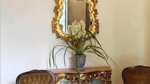 A room with a large ornate mirror, a wooden console table with a vase of flowers, and two upholstered chairs. - Casablanca Koeler Hotel (Petrópolis)