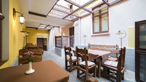 Un comedor con muebles de madera y un banco, una mesa con un florero, y un balcón con barandilla.