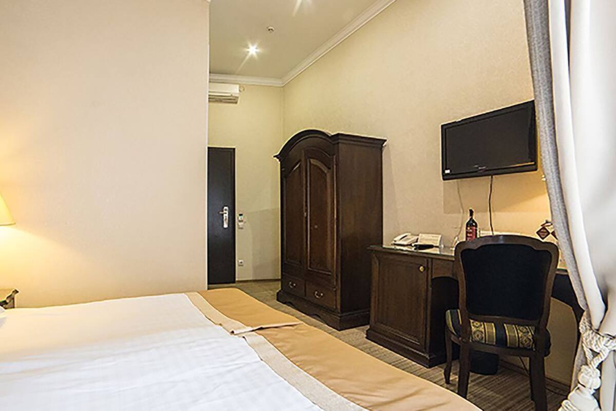 Habitación de hotel con cama, escritorio, silla, armario y televisor en la pared.