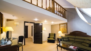 Habitación de hotel con escalera de madera, un sofá, una silla, un escritorio con teléfono y una lámpara.