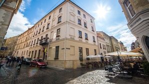 Un edificio histórico con múltiples ventanas, mesas al aire libre y una calle adoquinada.