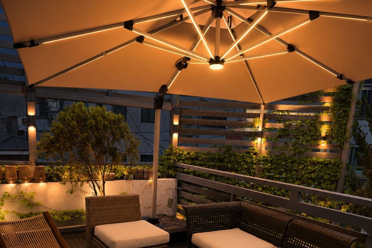 Een terras met rieten meubels, een salontafel met glazen blad en een grote parasol voor schaduw.