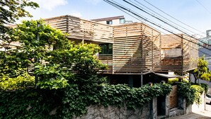 Un bâtiment moderne doté d’une façade en bois à lattes, d’un mur en pierre agrémenté de verdure et surplombé d’un ciel dégagé.