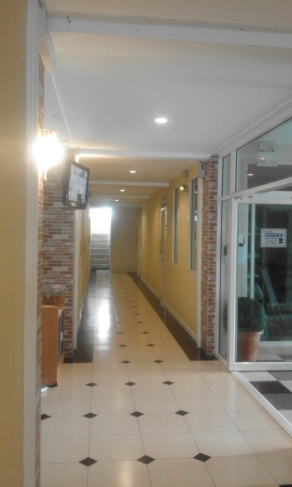 A corridor with tiled flooring, a brick wall on one side, and a glass door on the other.