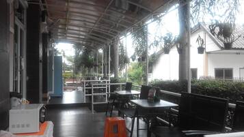 A covered outdoor seating area with tables and chairs, a coffee machine, and potted plants.