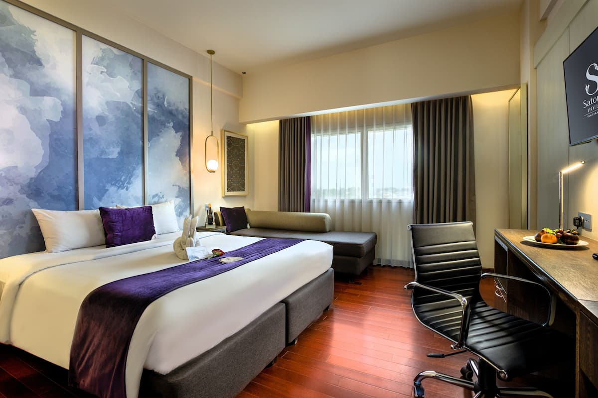 Habitación de hotel con una cama grande, un escritorio, una silla y vista a la ciudad.