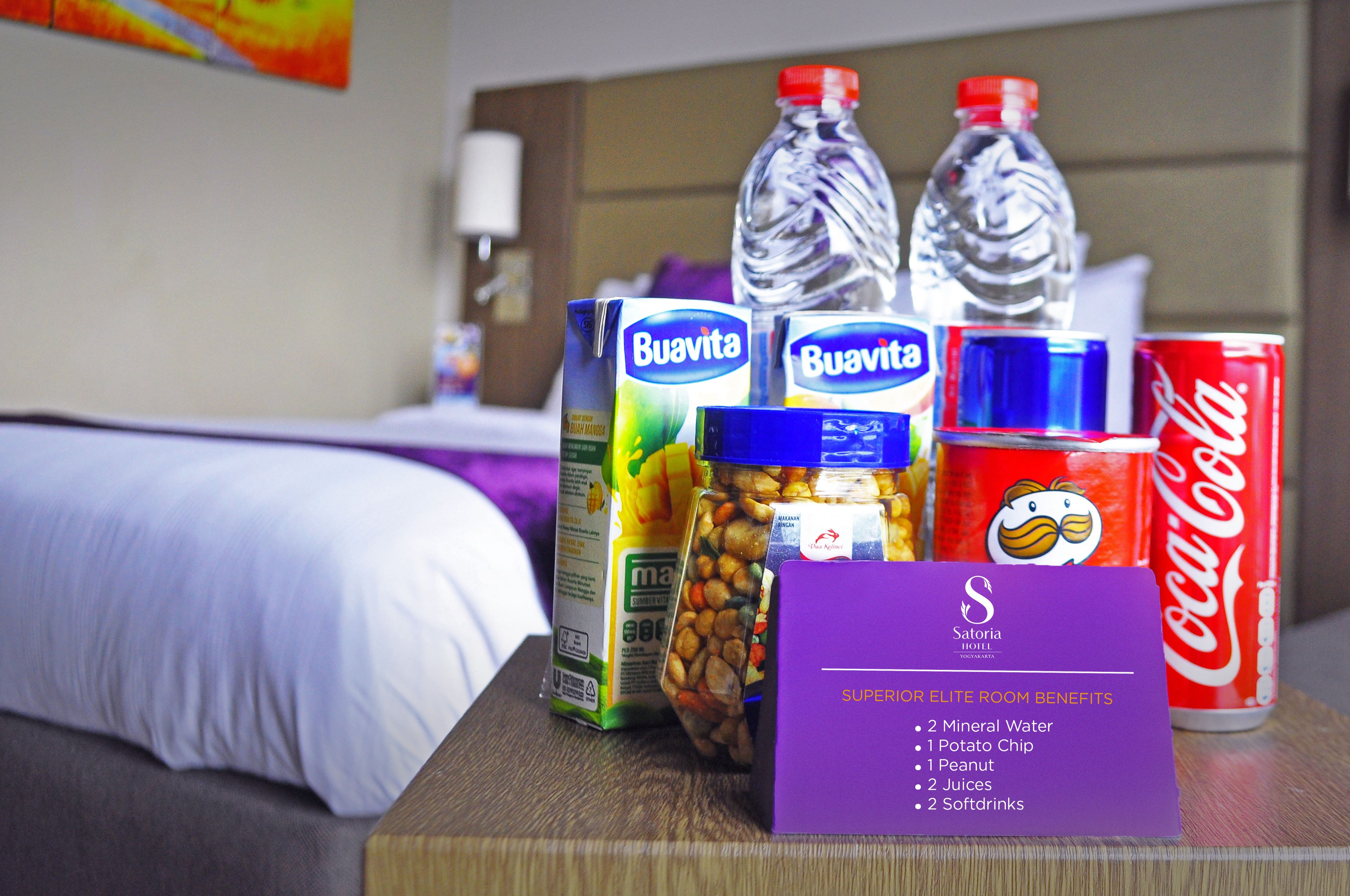 A hotel room with a bed, a wooden nightstand, and a sign listing room benefits.
