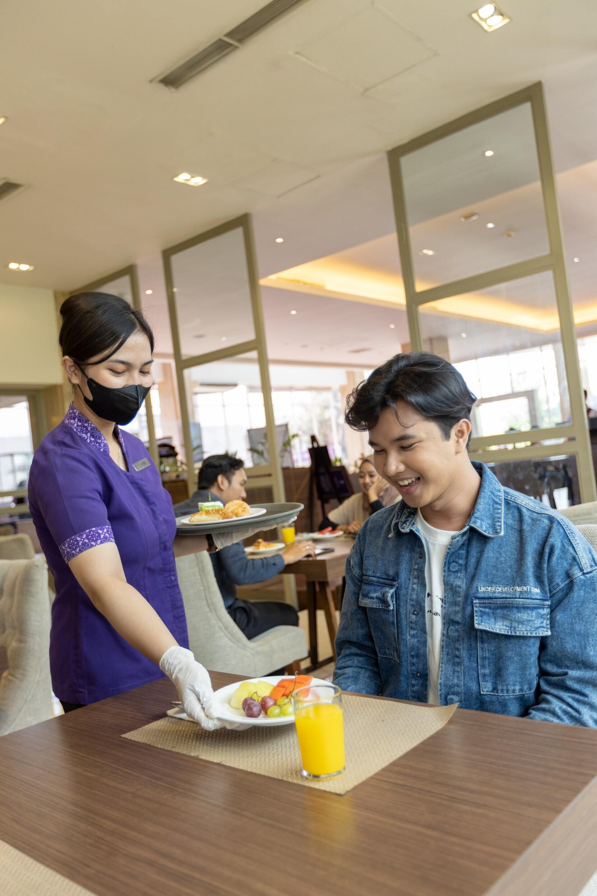 A hotel dining area with a waiter serving a meal to a guest.
