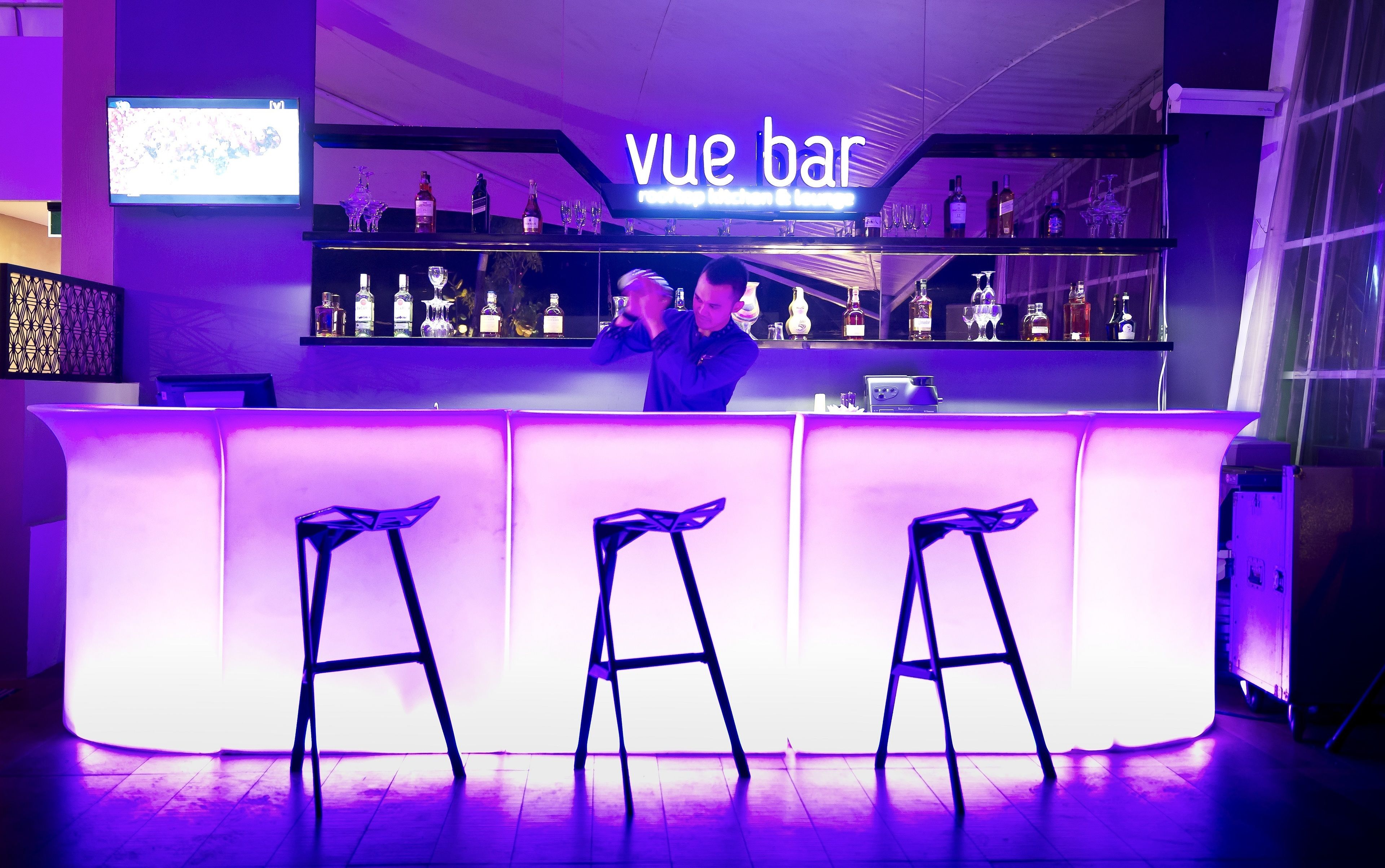A bar area with a neon sign reading "vue bar" and a bartender at the counter.