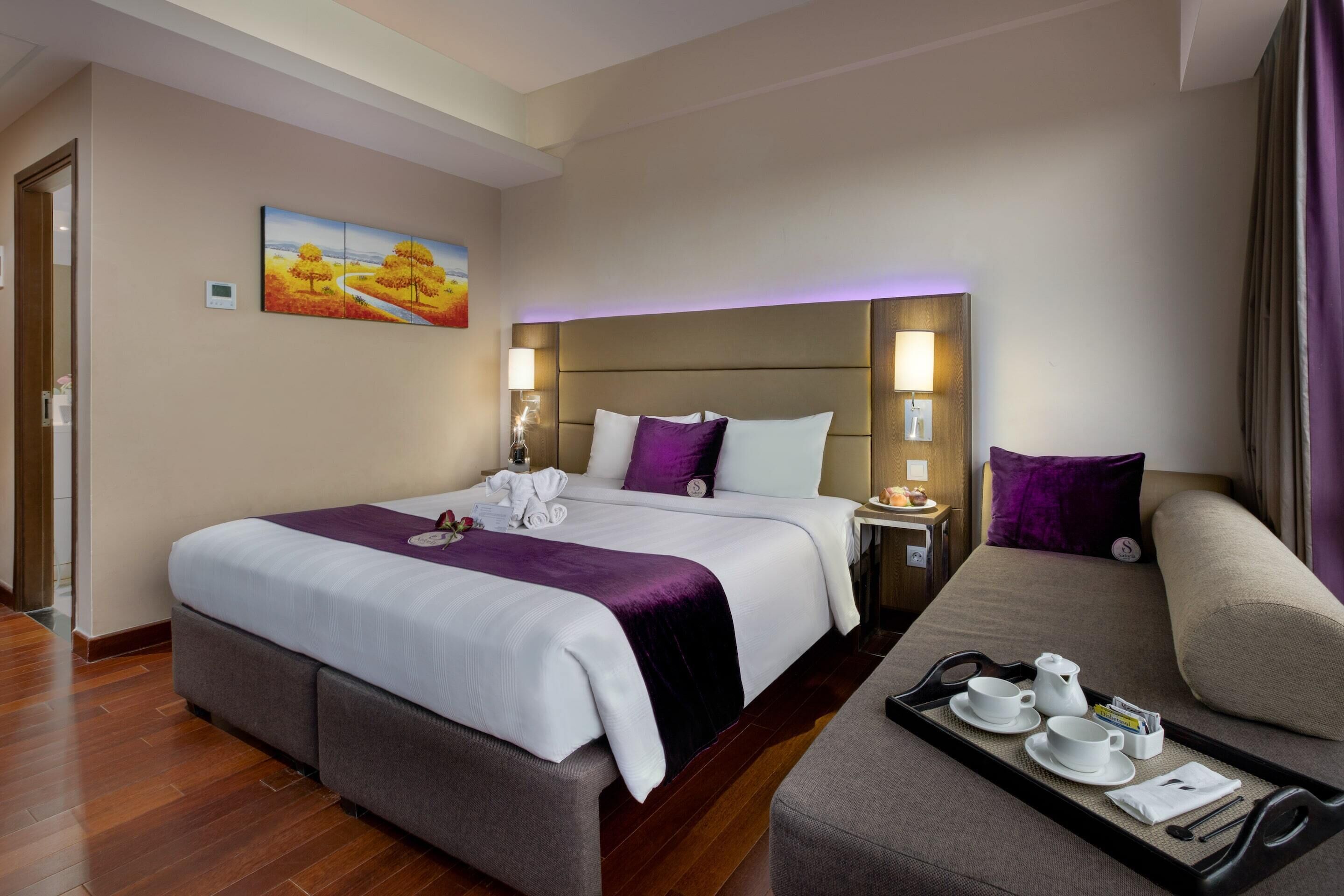 A hotel room with a large bed, a sofa, a tray with tea and a book, and a painting on the wall.