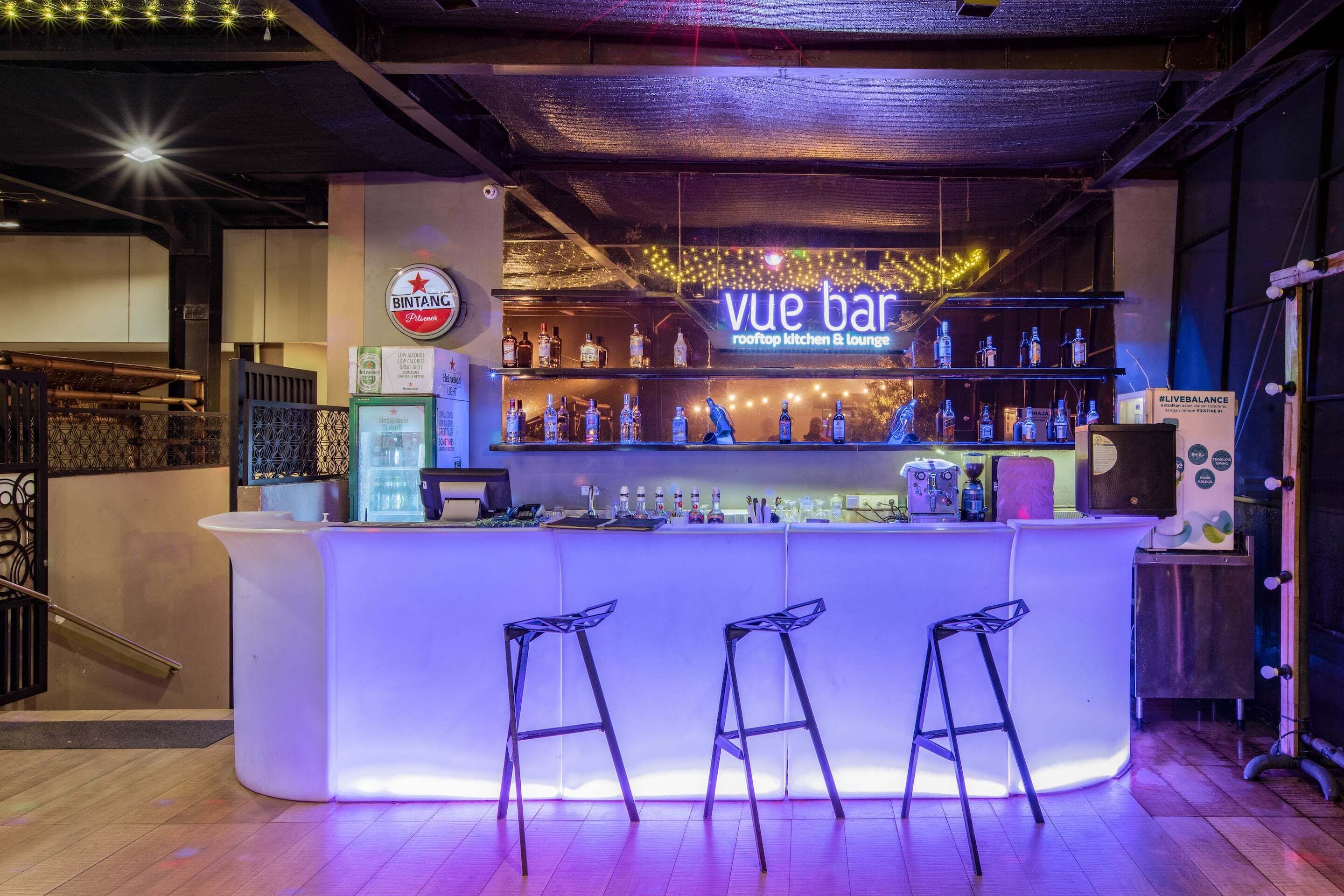 Eine Bar mit einer Neonreklame, Flaschenregalen und Barhocker.