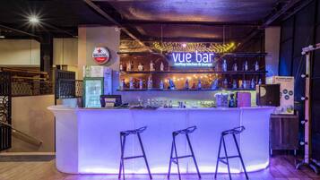 Eine Bar mit einer Neonreklame, Flaschenregalen und Barhocker.