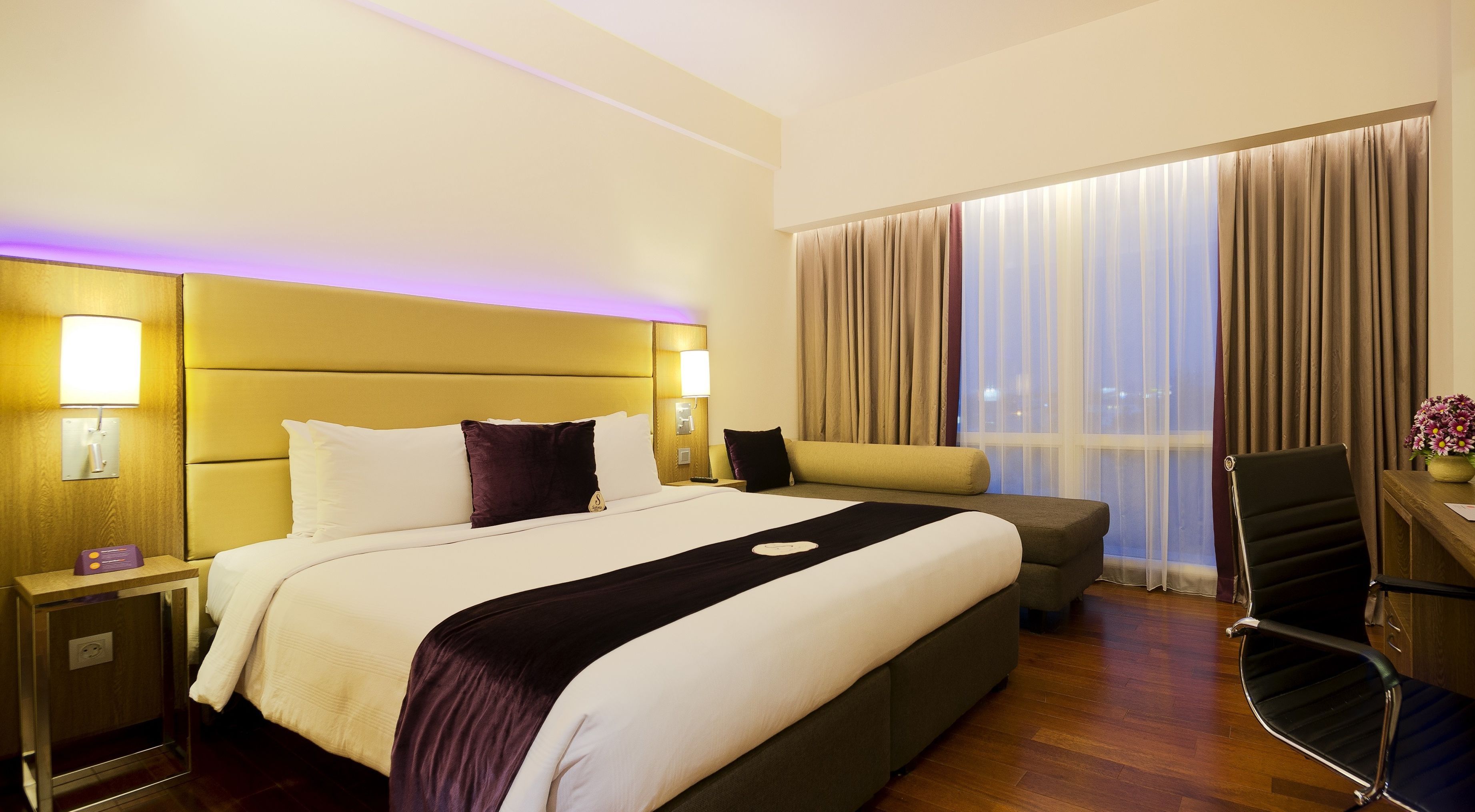 Habitación de hotel con una cama grande, mesitas de noche, un escritorio, una silla y vista a la ciudad por la ventana.