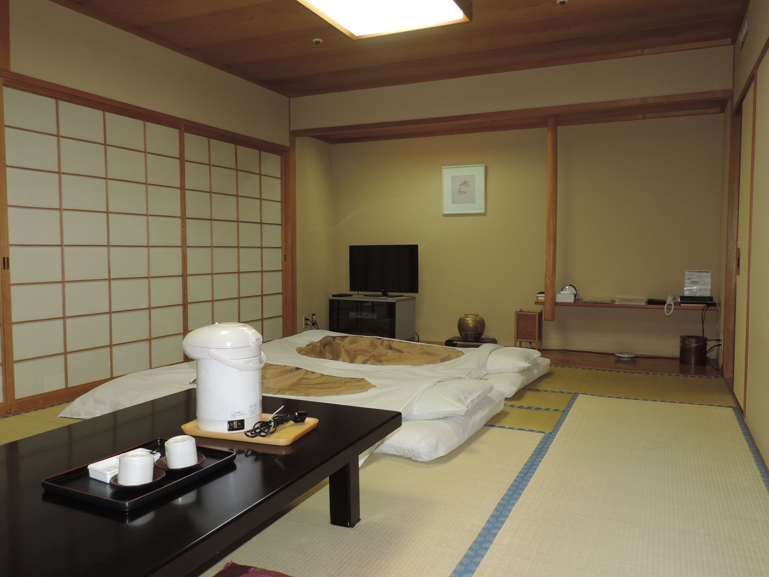 Una habitación japonesa tradicional con suelo de tatami, un futón, un televisor y una bandeja con tazas y un hervidor.