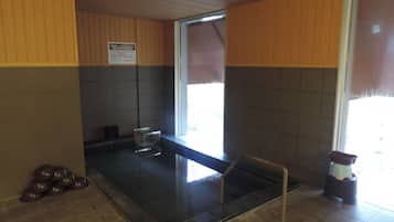 A sauna room with a tiled floor, a glass container, and a wooden bench.