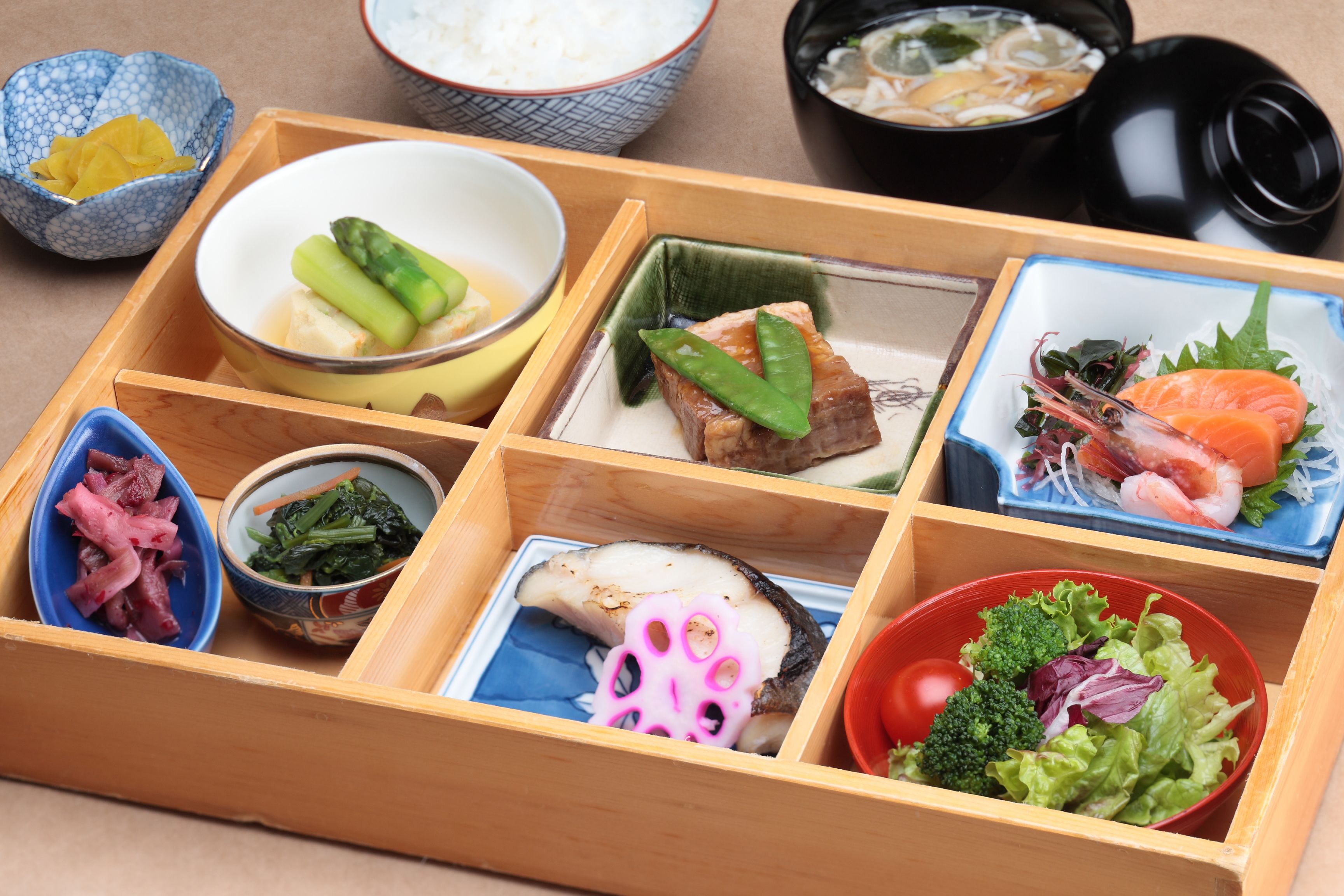 Una caja de almuerzo de madera con varios compartimentos que contienen diferentes alimentos.