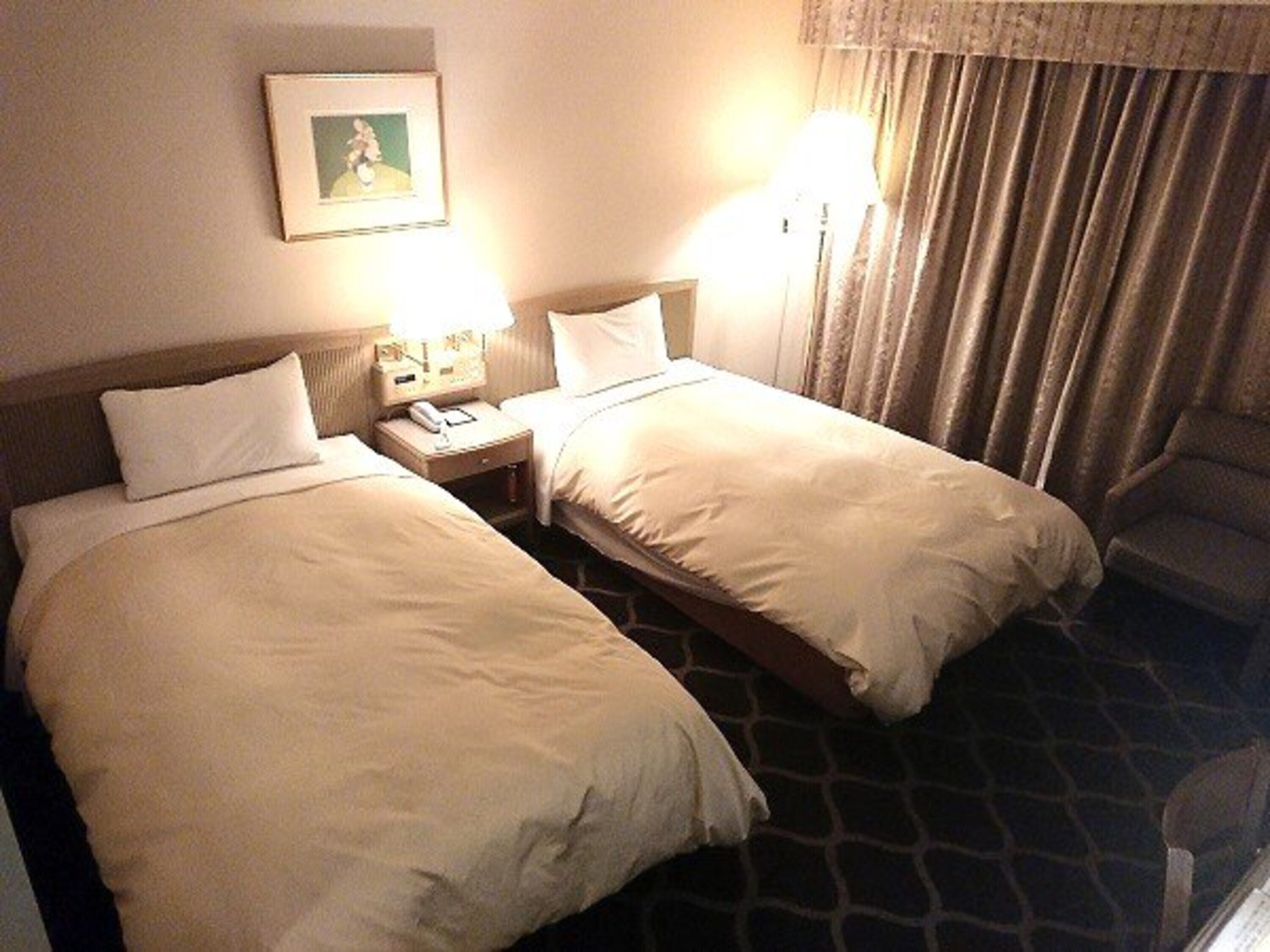 A hotel room with two beds, a nightstand with a phone, a lamp, and a picture on the wall.