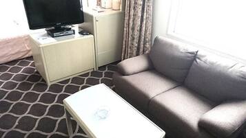A hotel room with a grey sofa, a small white table, a TV on a cabinet, and patterned carpet.