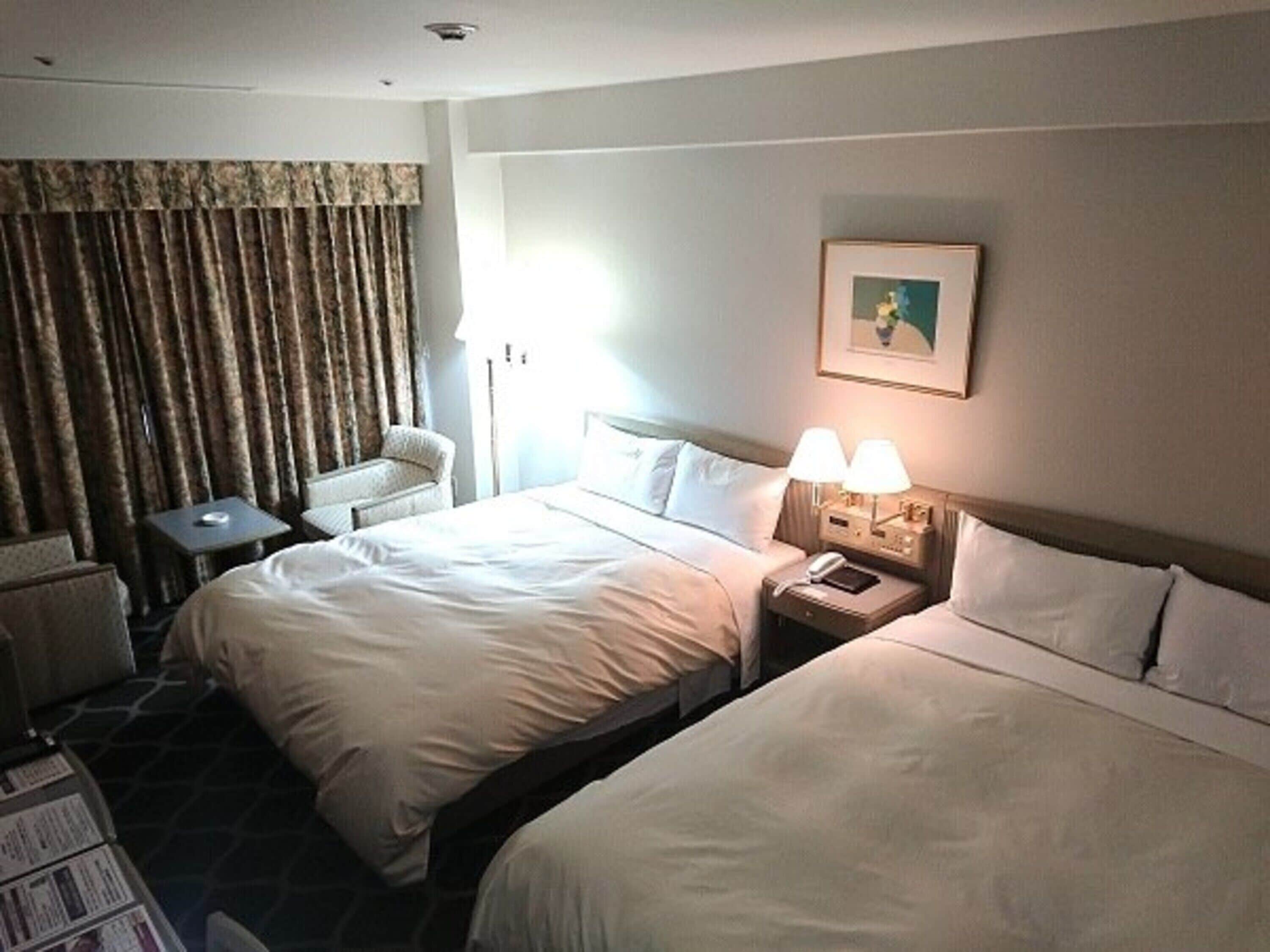 Een hotelkamer met twee bedden, een bureau, een stoel en een lamp.