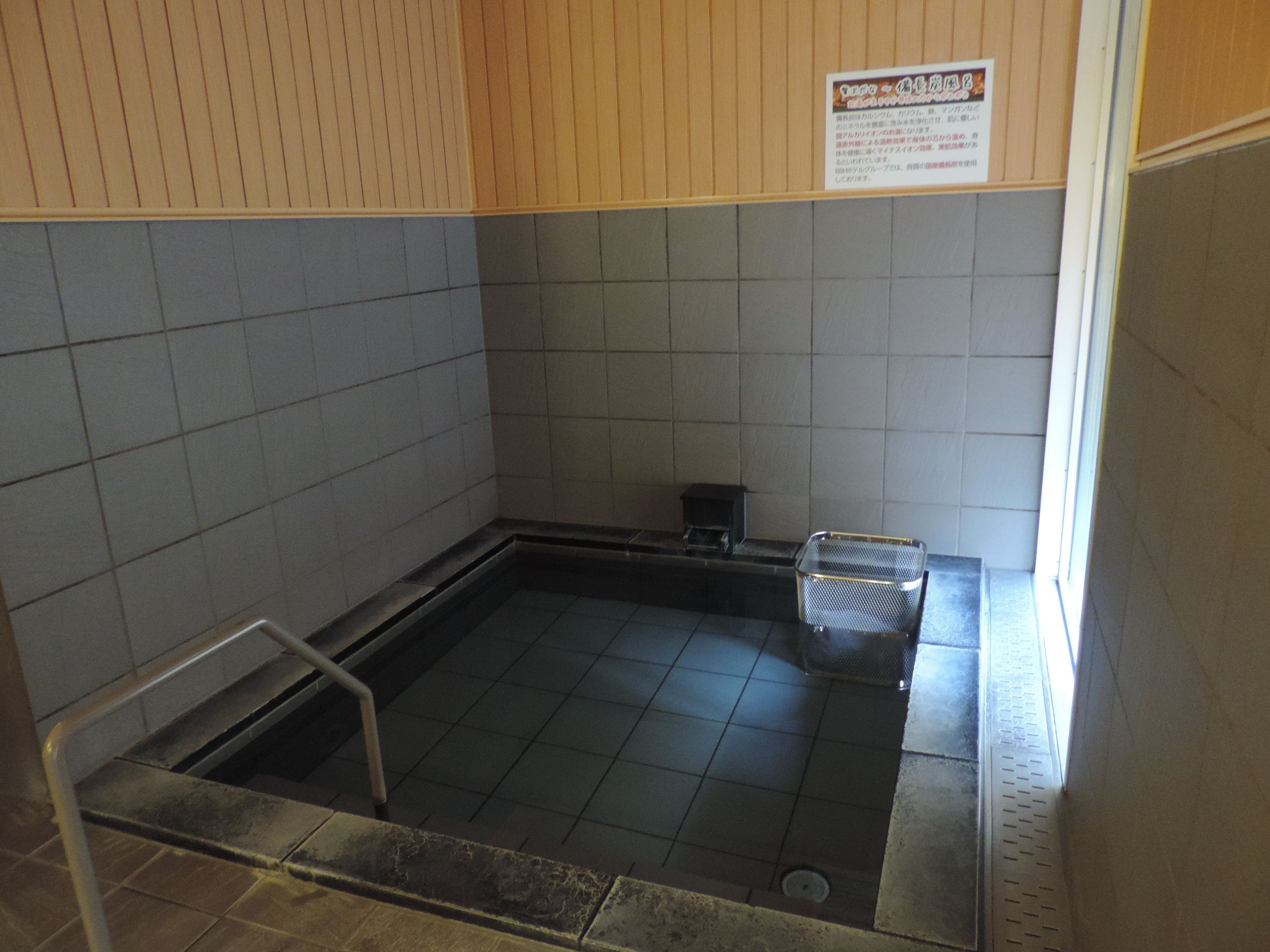 A small, tiled room with a metal bench and a trash bin.