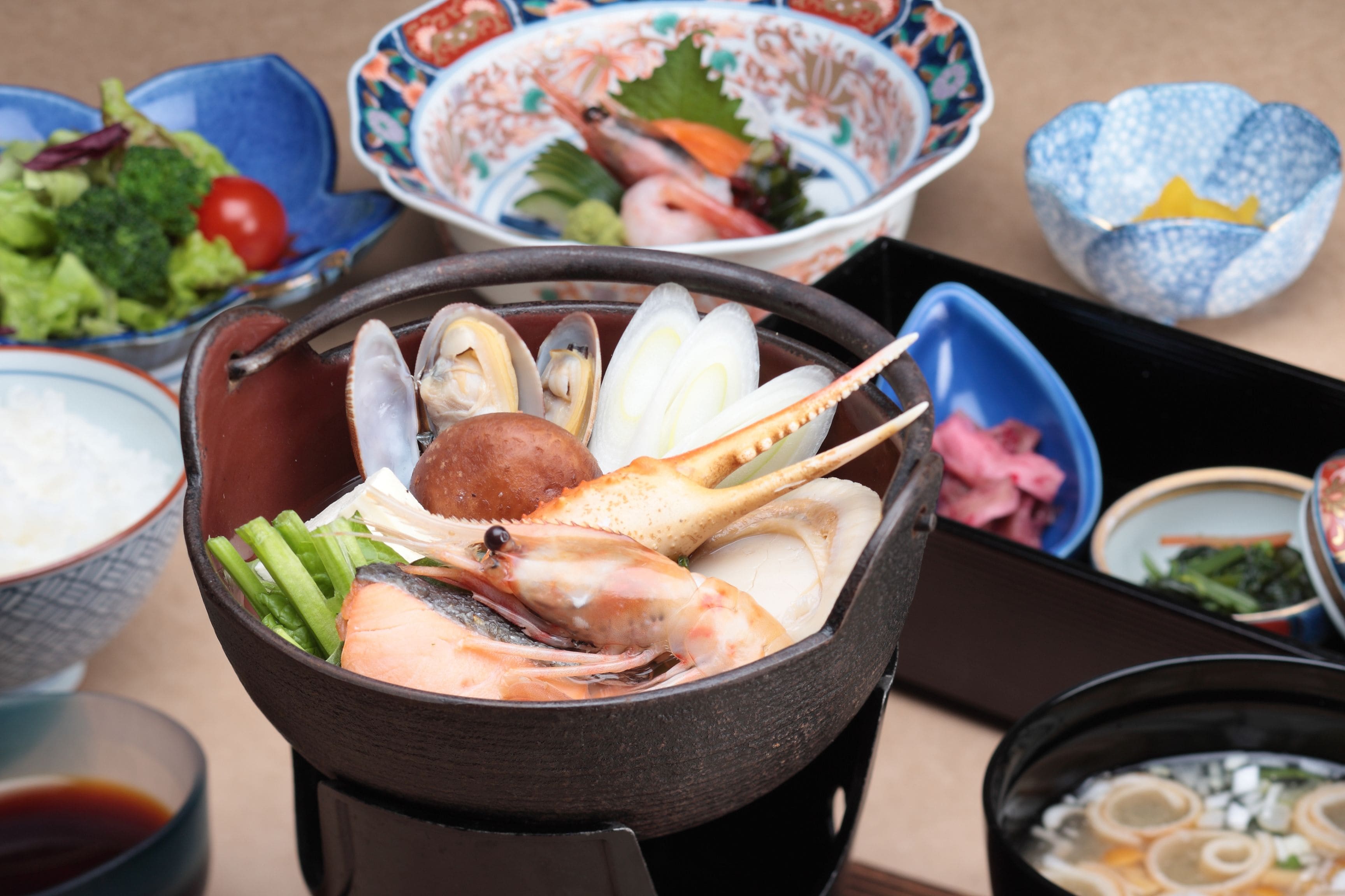 Diverse gerechten, waaronder zeevruchten, groenten en rijst, geserveerd in traditionele schalen en een warme pot.