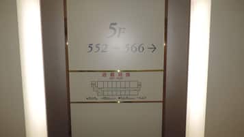 Letrero de número de habitación de hotel con '5F' y '552-566' que indica el rango de habitaciones. Abajo, un plano de planta con 'PLAN DE SALIDA' y 'SALIDA DE EMERGENCIA' marcados.