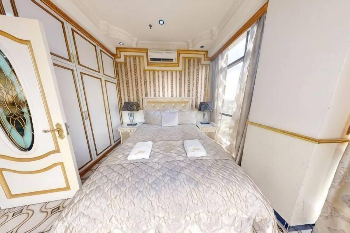 A bedroom with a large bed, two bedside tables, a headboard, and a window.