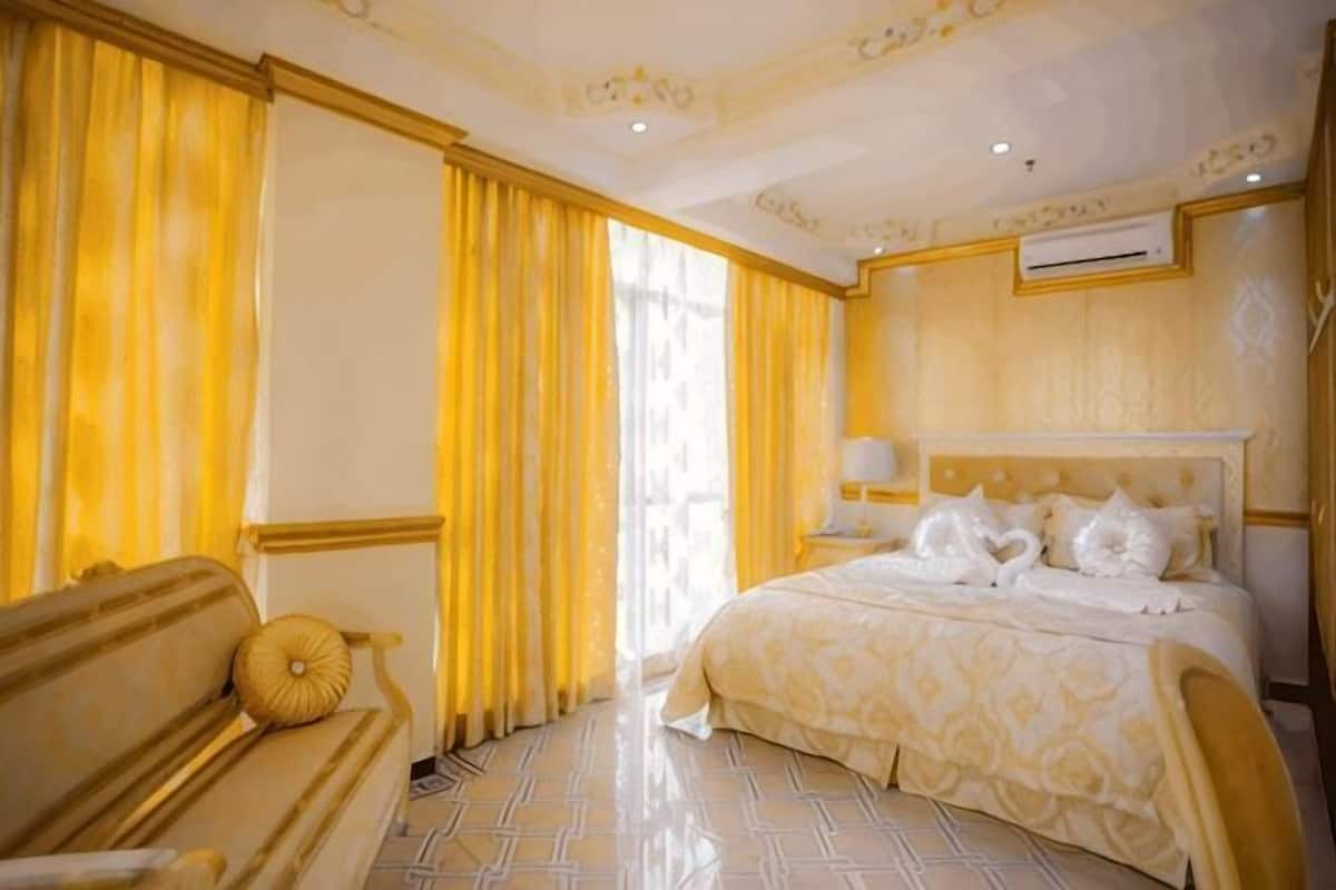 A hotel room with a bed, a sofa, curtains, and a window.