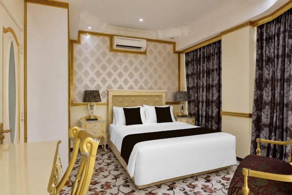Habitación de hotel con cama, mesitas de noche, una silla y un detalle decorativo en la pared.