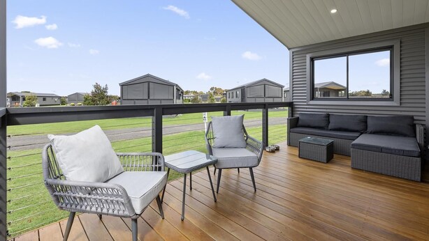 A covered outdoor area with wicker furniture, a wooden deck, and a view of houses in the background. - Swan Bay Holiday Park (Swan Bay)