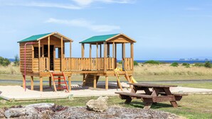 Two wooden playhouses with green roofs and a picnic table in a grassy area with a clear sky. - Swan Bay Holiday Park (Swan Bay)