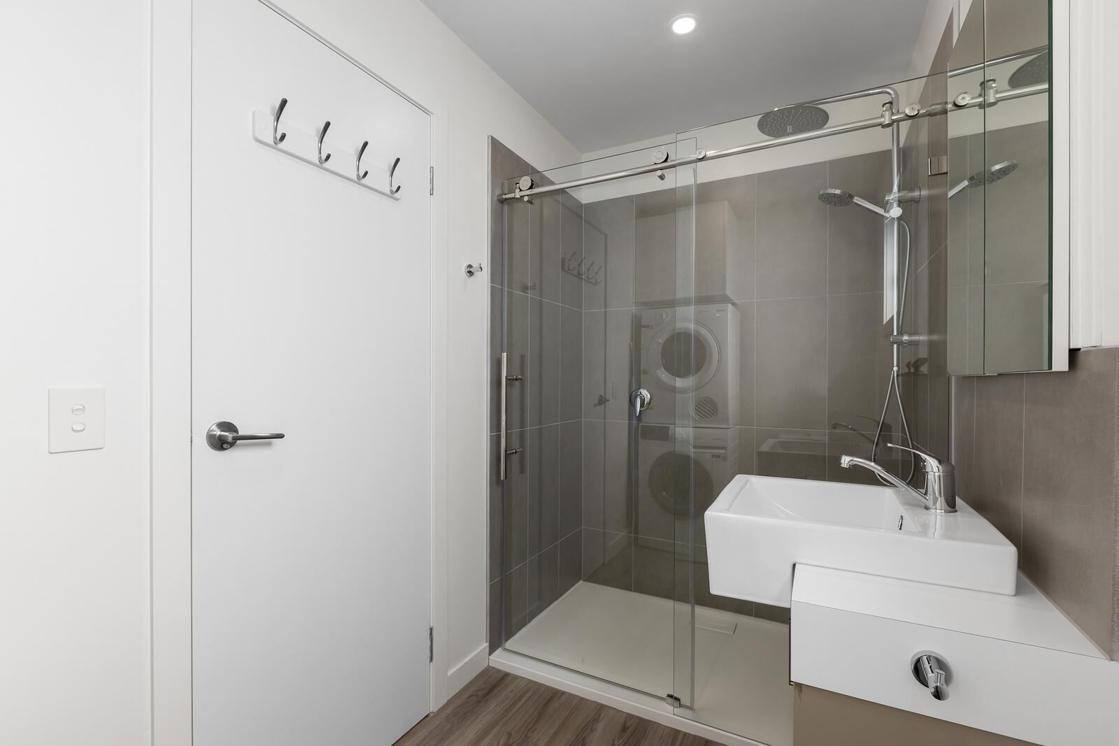 A modern bathroom with a glass-enclosed shower, a white sink, and a built-in washing machine.