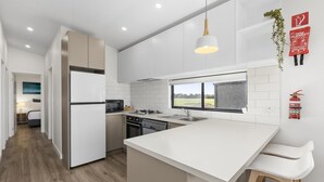 A modern kitchen with white cabinetry, a central island, a microwave, a stove, and a sink. There is a window providing a view of the outdoors. - Swan Bay Holiday Park (Swan Bay)