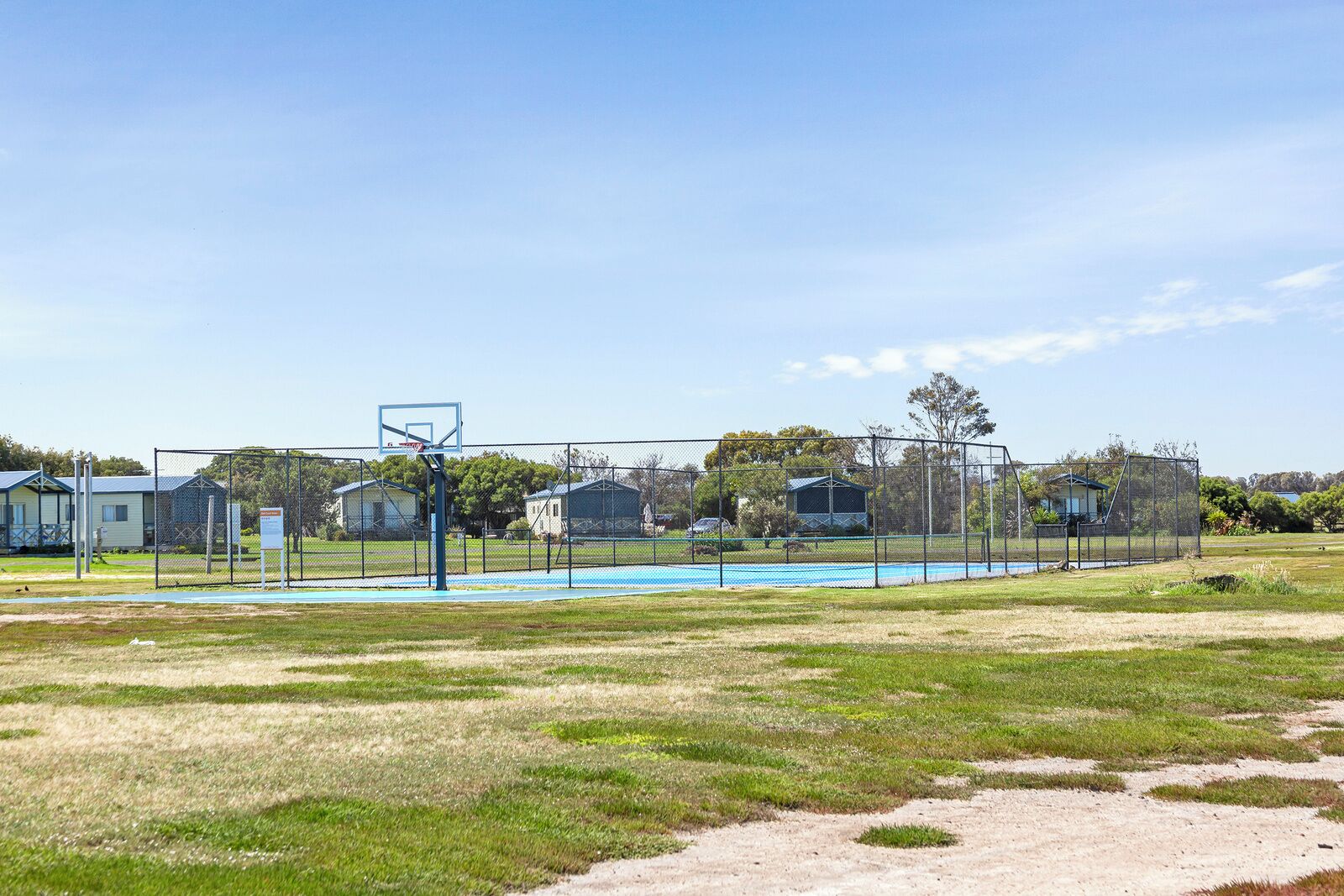Una cancha de baloncesto al aire libre con valla, rodeada de casas y árboles.
