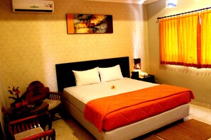 A hotel room with a bed, a nightstand, a desk, and a chair. - Crown Hotel (Mataram)