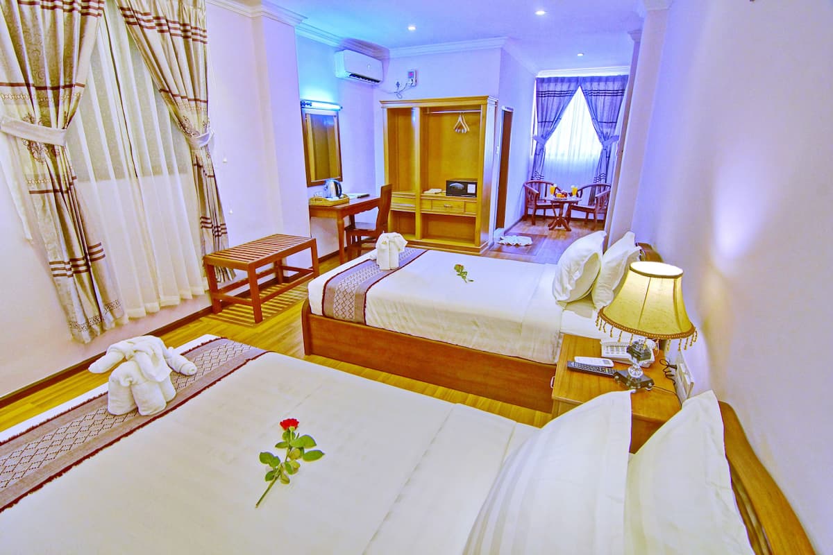 A hotel room with two beds, a desk, a chair, a wardrobe, and a bathroom visible in the background.