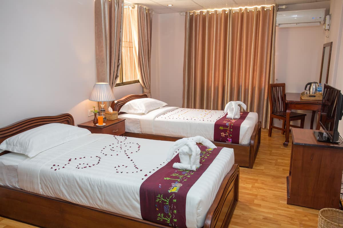 A hotel room with two beds, a desk, a chair, a lamp, and an air conditioning unit.