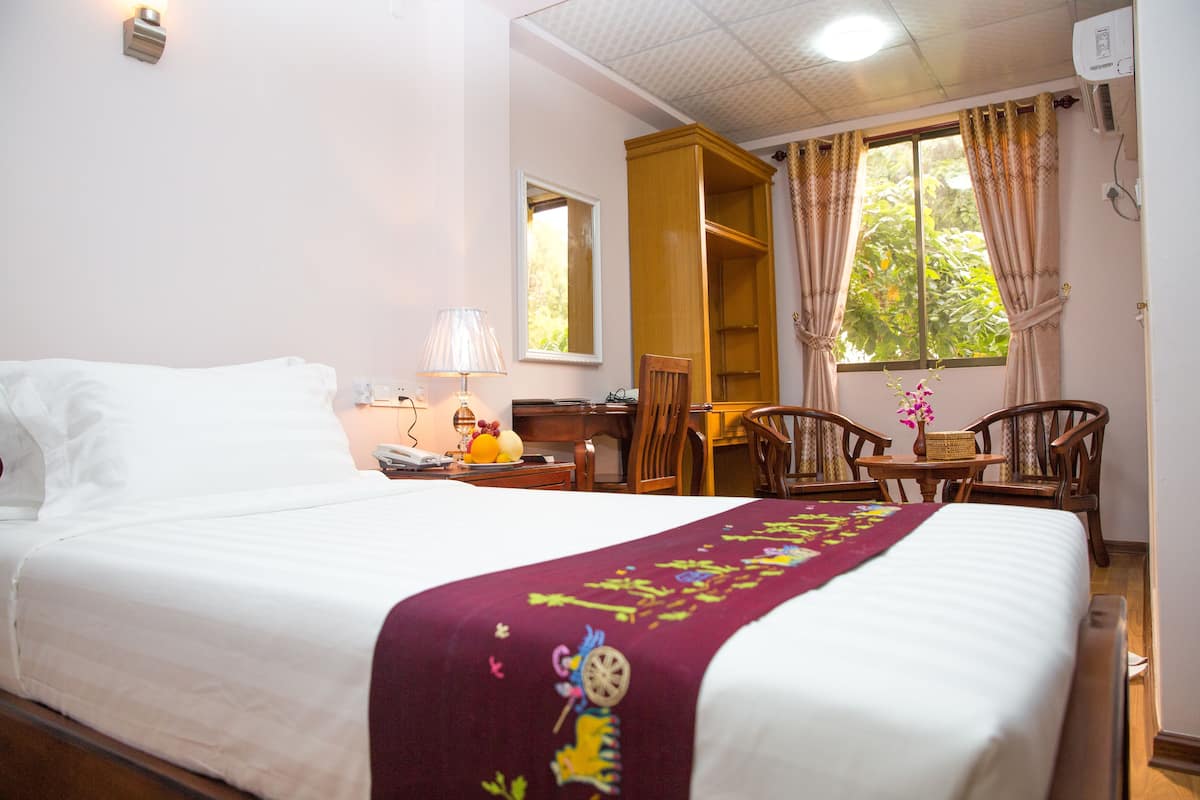 A hotel room with a bed, a desk, a chair, and a window with curtains.