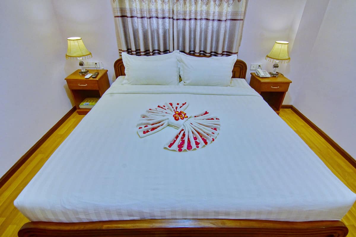 A neatly made bed with a decorative towel on the center, two bedside tables with lamps, and a window with curtains.