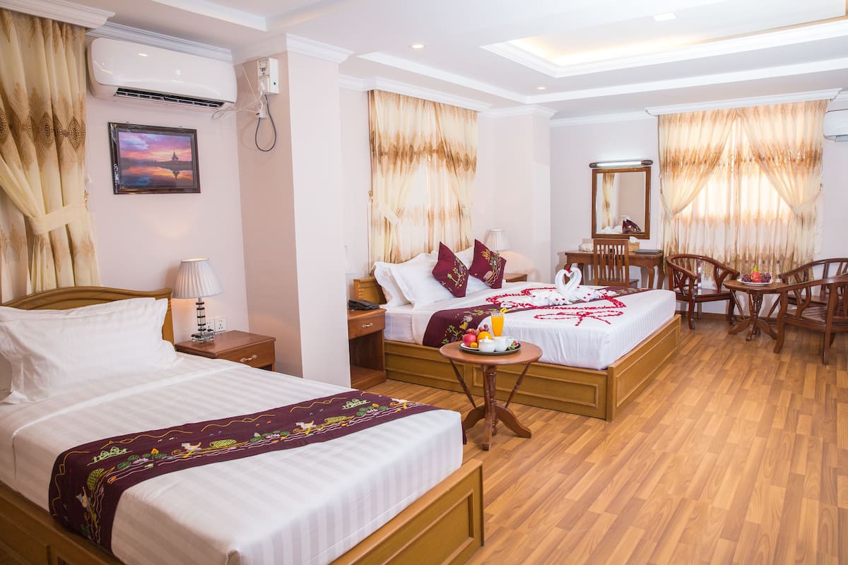 A hotel room with two beds, a wooden floor, a desk, a chair, a mirror, and a picture on the wall.