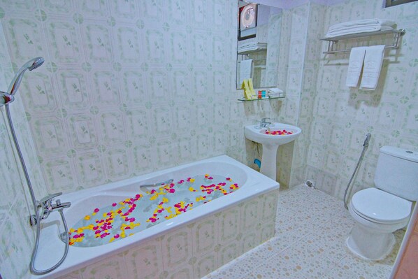 A bathroom with a bathtub filled with rose petals, a sink, a toilet, and a shower.