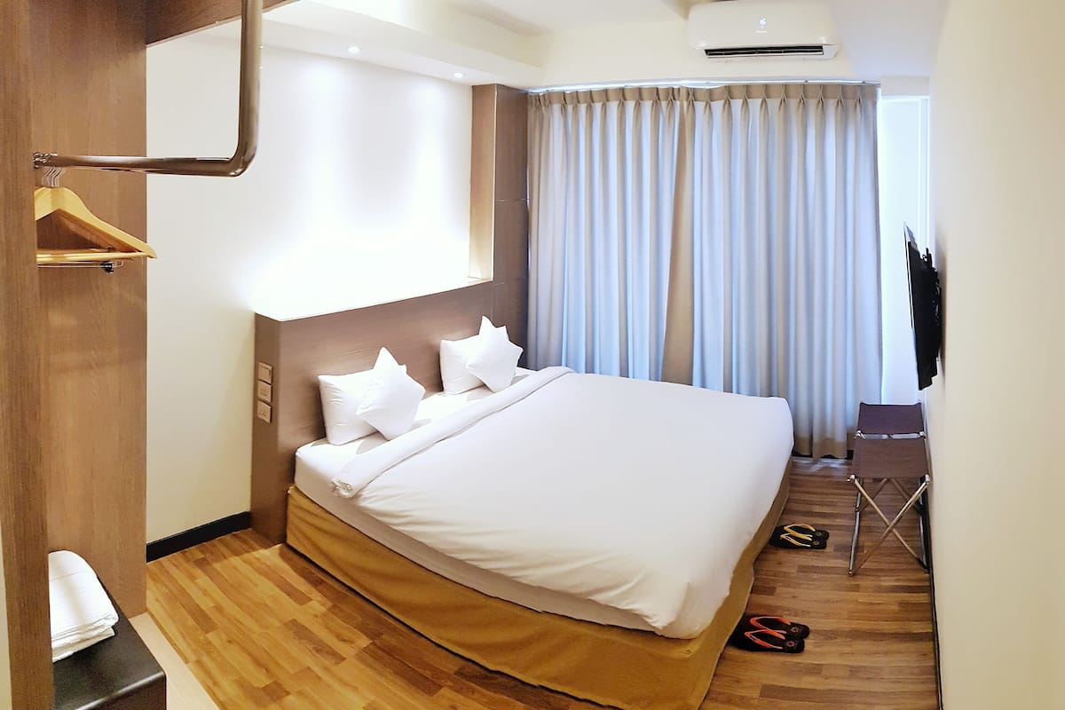 A hotel room with a large bed, a wooden wardrobe, a desk, and a TV.