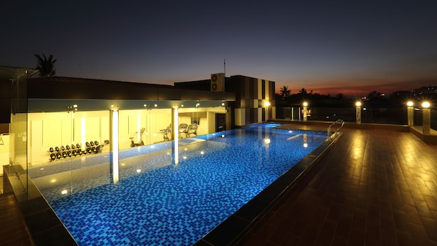 A swimming pool with a blue mosaic tile floor, surrounded by a building with a modern design, including a seating area with chairs and a small table. - Clover Suites Royal Lake Yangon (Yangon)