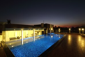 A swimming pool with a blue mosaic tile floor, surrounded by a building with a modern design, including a seating area with chairs and a small table. - Clover Suites Royal Lake Yangon (Yangon)