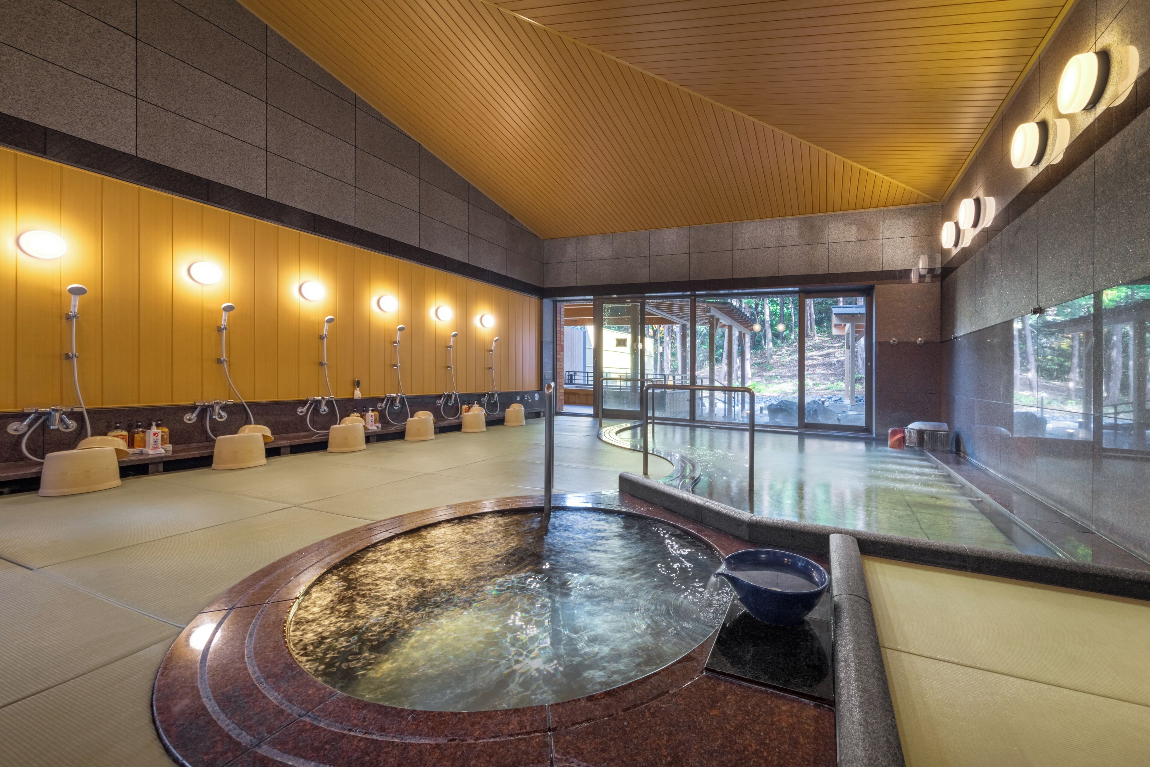 Un área de spa moderna con una bañera de hidromasaje central, múltiples cabezales de ducha y una amplia entrada de vidrio.