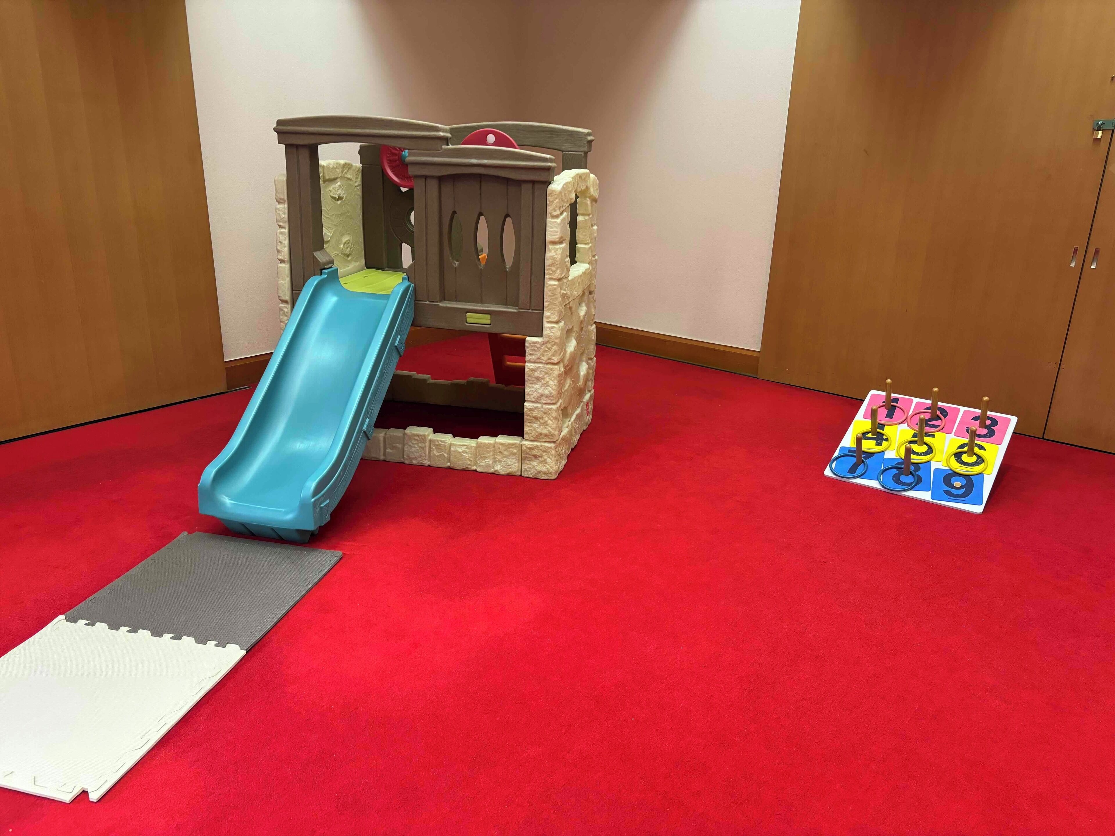Un espace de jeux avec un toboggan, une petite structure d’escalade et un jeu de société sur le sol.