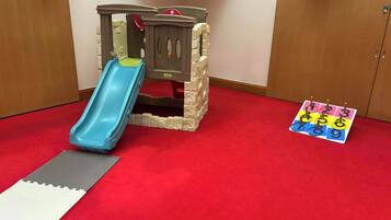 Un espace de jeux avec un toboggan, une petite structure d’escalade et un jeu de société sur le sol.