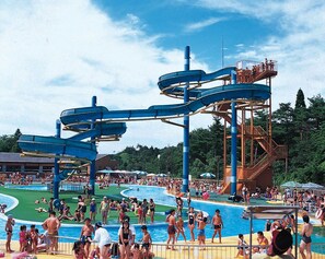 Parque acuático con toboganes y piscinas, rodeado de árboles y un cielo despejado.