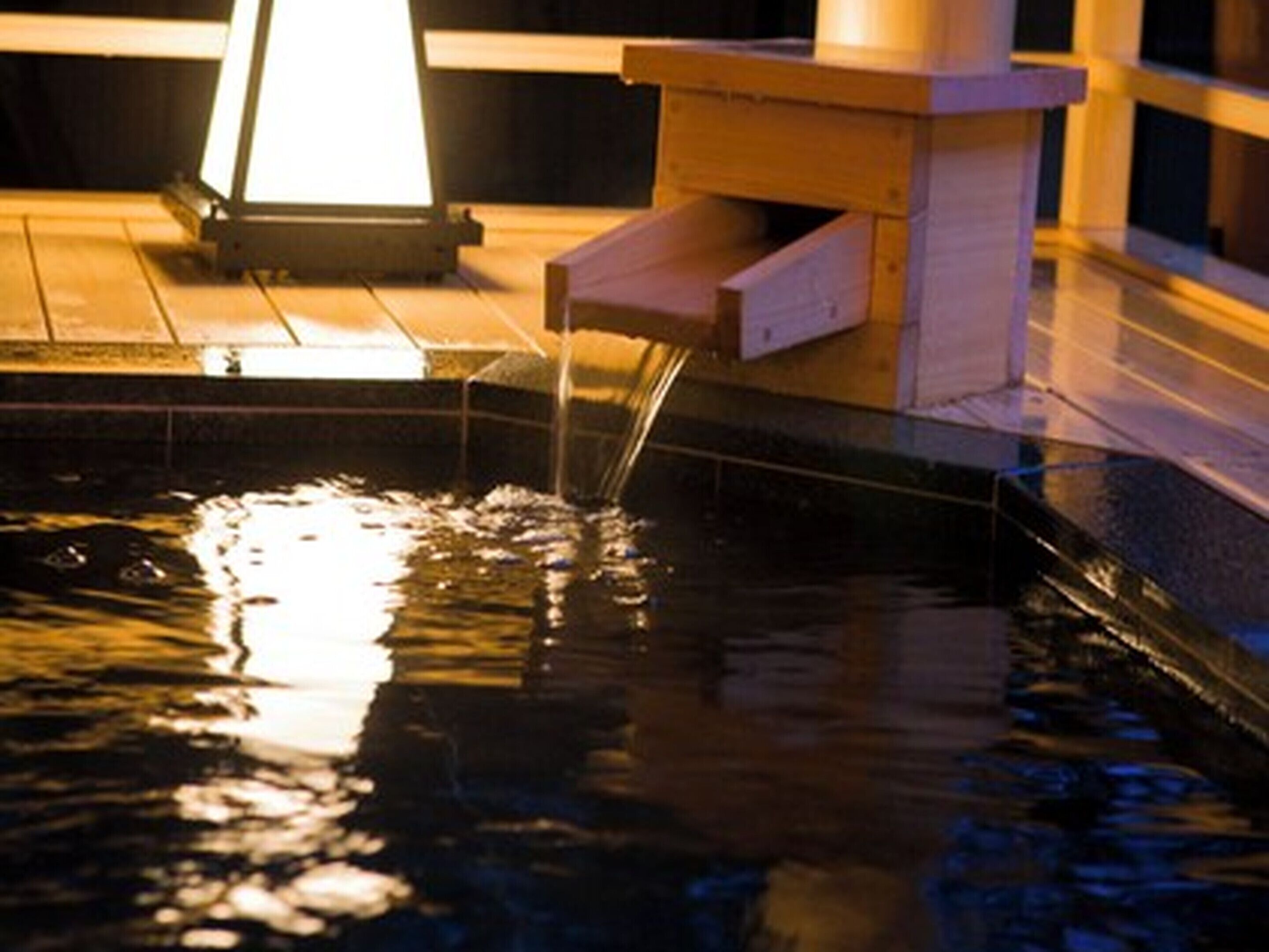 A pool with water flowing into it, surrounded by wooden deck and a light fixture above.